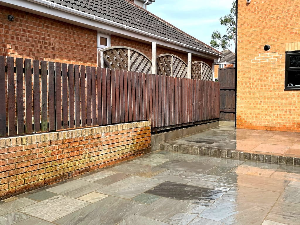 Wet sandstone paving running to a red brick wall behind a slatted timber fence