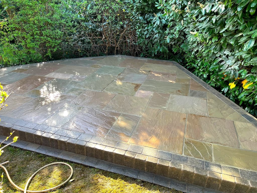 Raised sandstone patio with a sett edge set against a tall green hedge