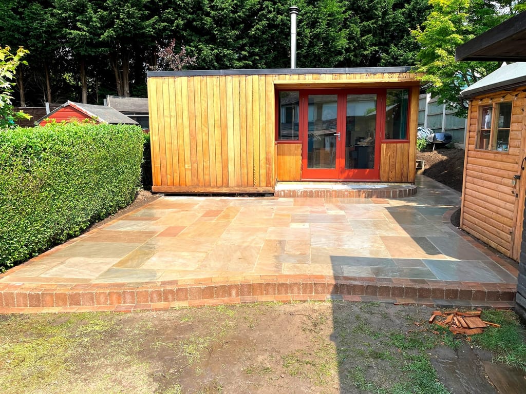 Raised sandstone patio and cedar garden room seen from across the lawn