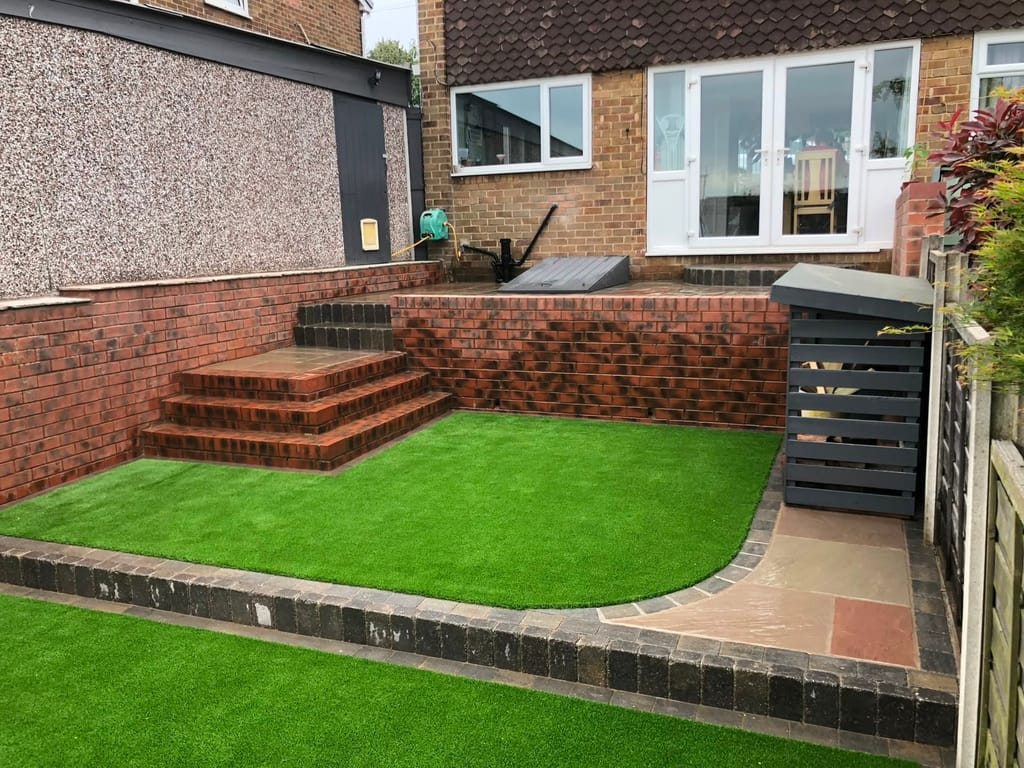 Artificial lawn below a red brick retaining wall with brick steps up to the house