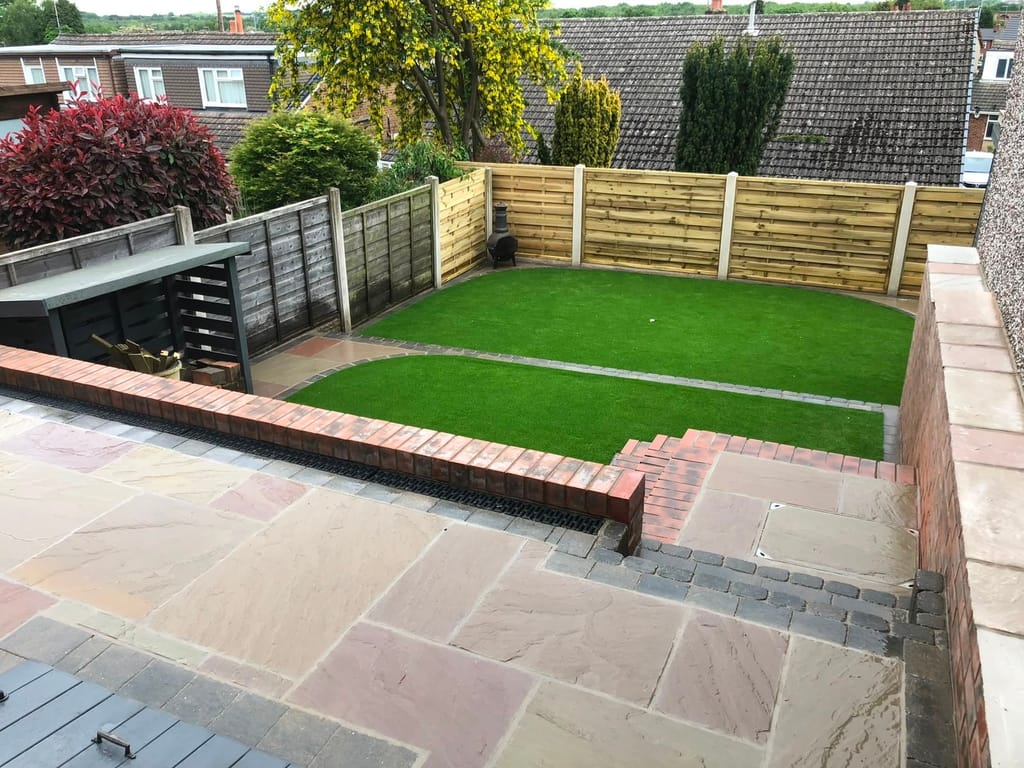 Raised artificial lawn behind red brick walls above a sandstone patio