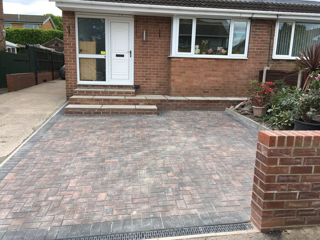 Herringbone block driveway with a channel drain across the mouth and sandstone steps to the front door