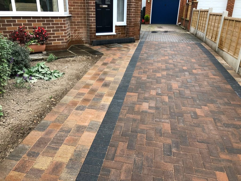 Herringbone block driveway with a charcoal border running down the side of a house to a blue garage door