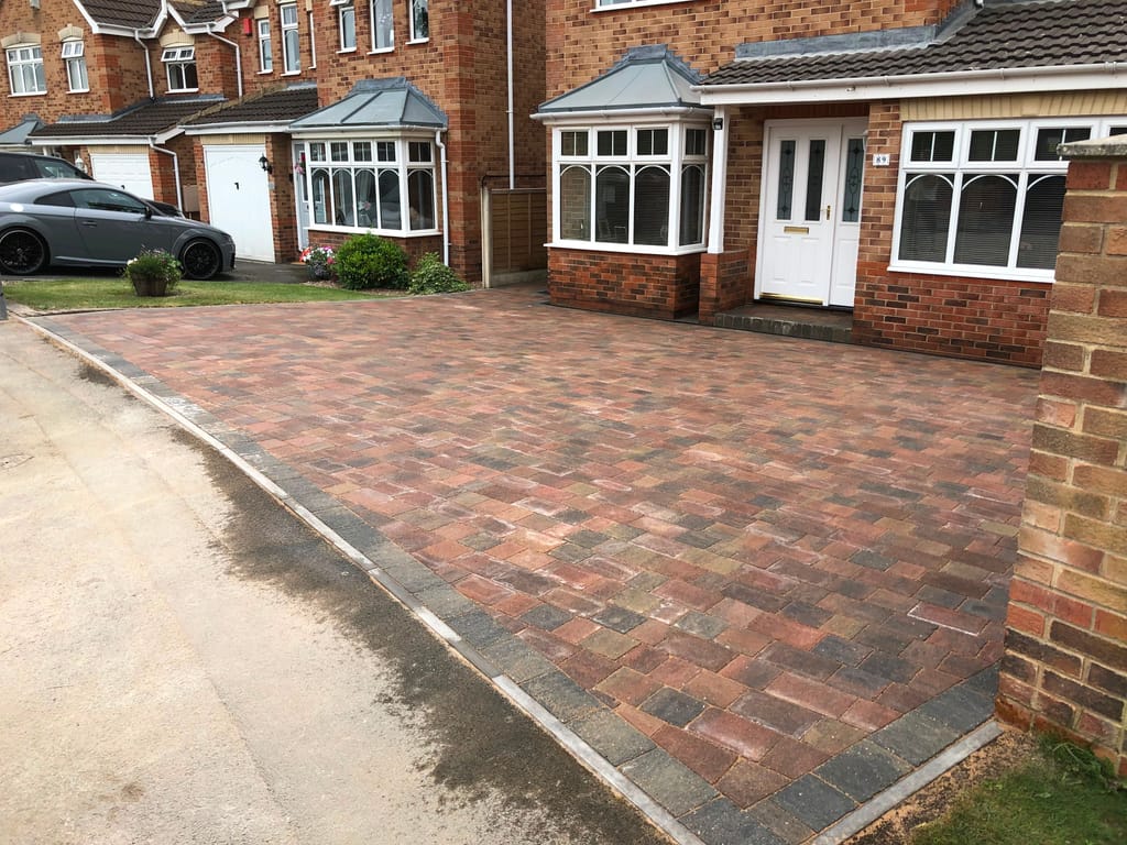 Wide brindle block driveway laid to the kerb at a red brick house with twin bay windows