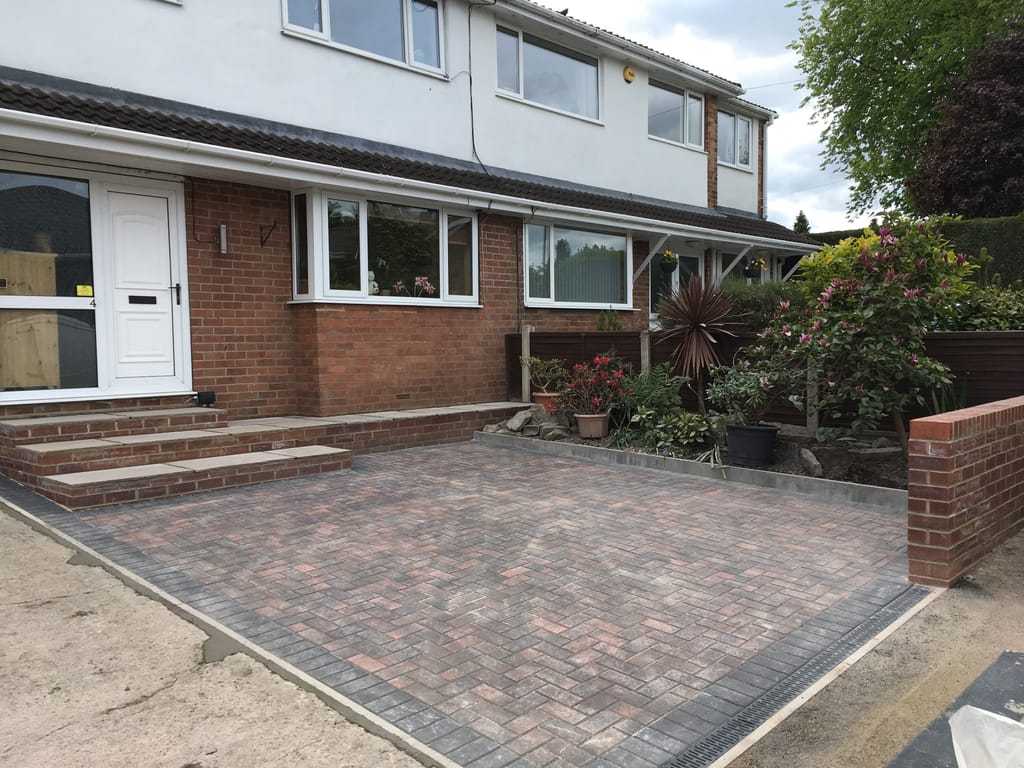 Block paved driveway with a charcoal border and brick steps up to the door of a rendered semi