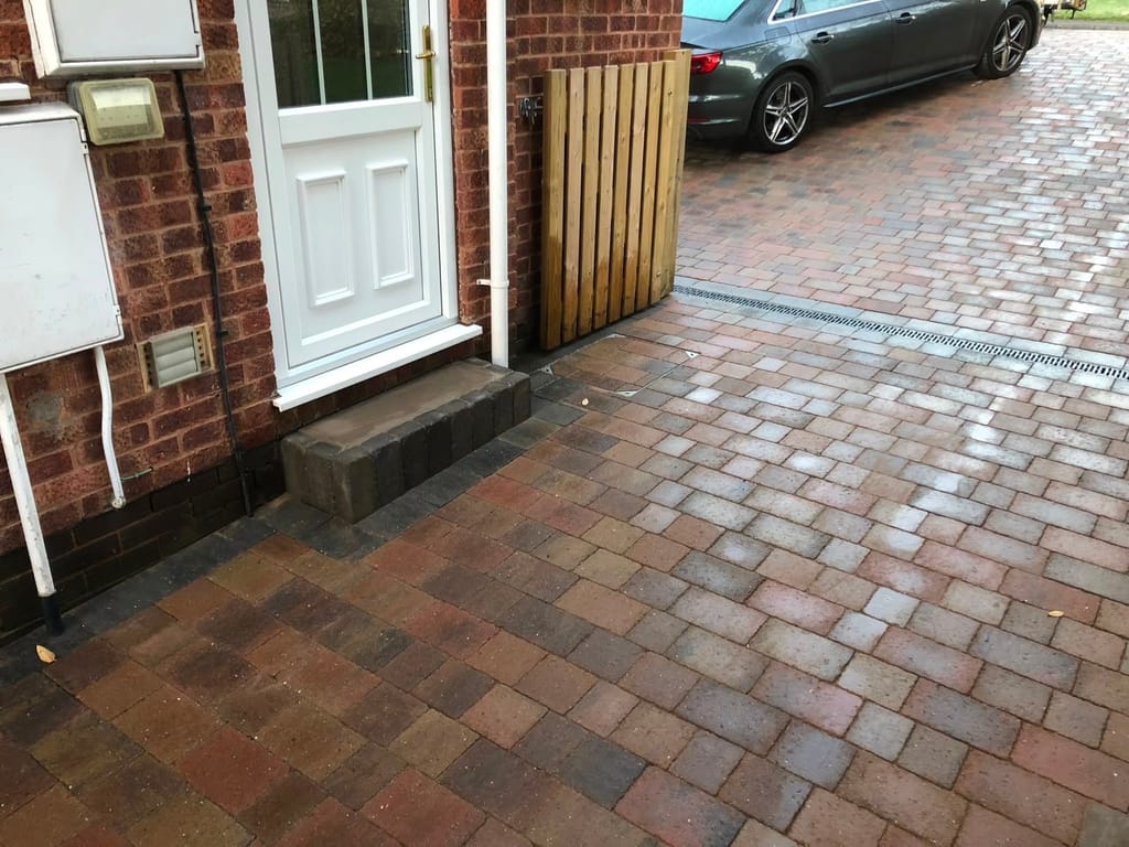 Block paving at a side door with a new timber gate, a charcoal step and a channel drain