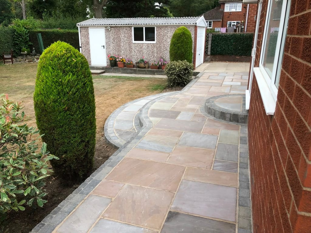 Sandstone path with charcoal sett edging curving past a lawn to a garden outbuilding