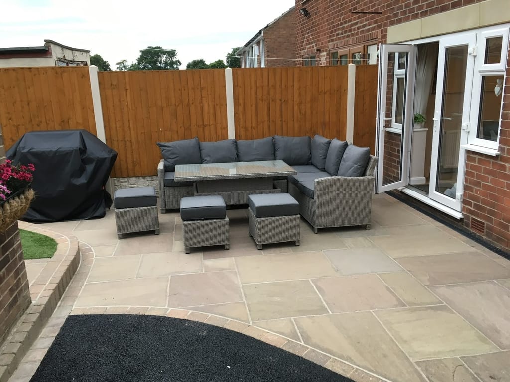 Sandstone patio laid out with a grey rattan corner sofa beside white french doors