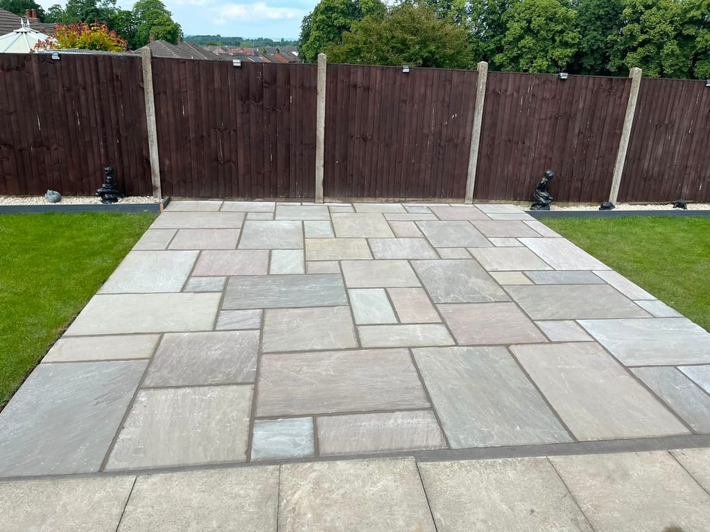 Sandstone patio squared off between two lawns in front of a dark stained close board fence