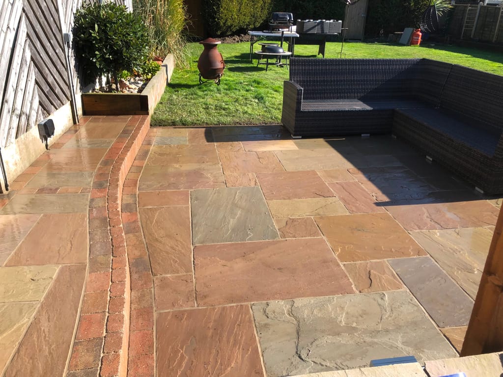 Sandstone terrace with a sweeping brick paved band, a raised timber planter and a corner sofa