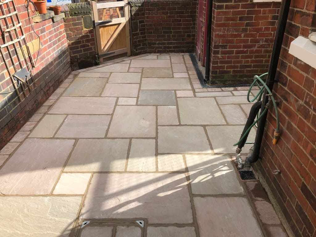 Sandstone paving in a walled rear yard with a timber gate at the far end