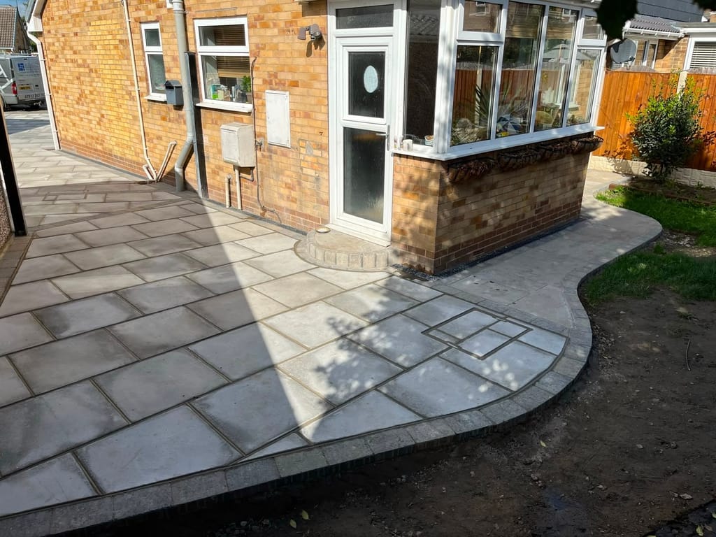 Cream slab patio with a charcoal border curving round a bungalow conservatory