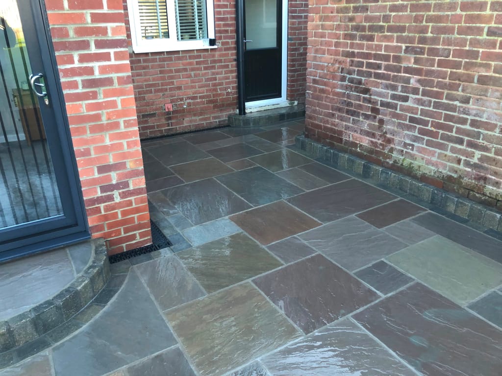 Sandstone paving in a brick corner with a curved sett step at grey french doors