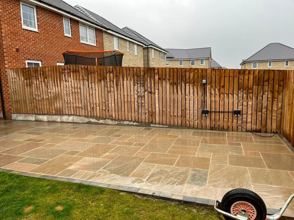 Sandstone patio filling a new build rear garden up to a close board fence and gate