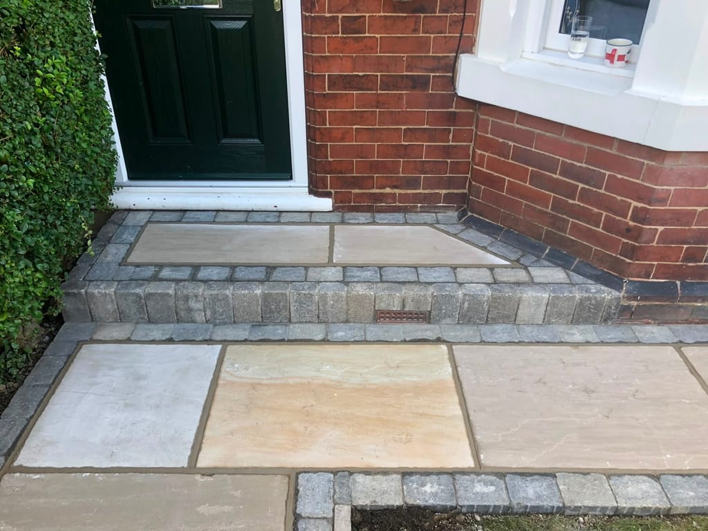 Sandstone doorstep and paving with sett borders at a dark green front door