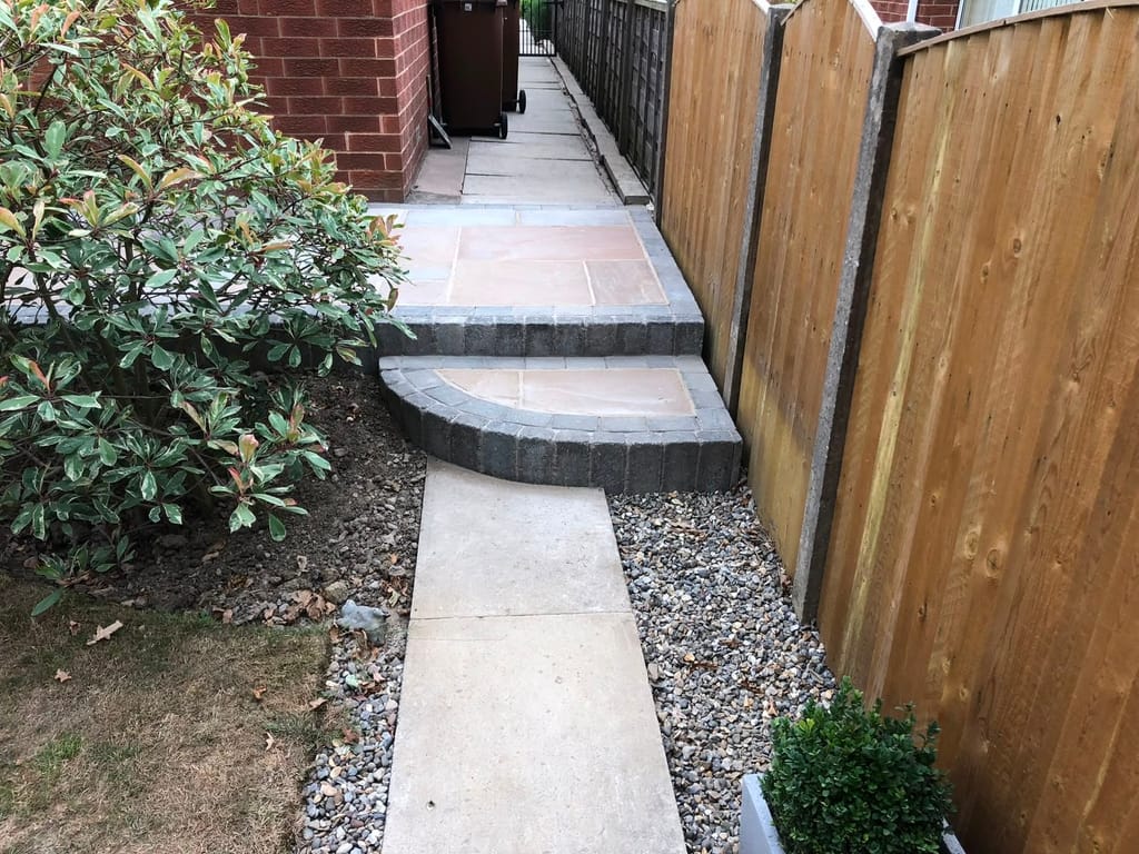 Curved sett edged step lifting a sandstone path in a narrow fenced side passage