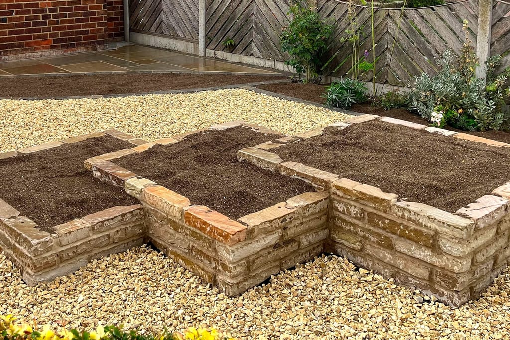 Raised brick planting beds built into a gravel front garden at a brick bungalow